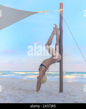 Woman doing handstand on beach in hat Banque D'Images