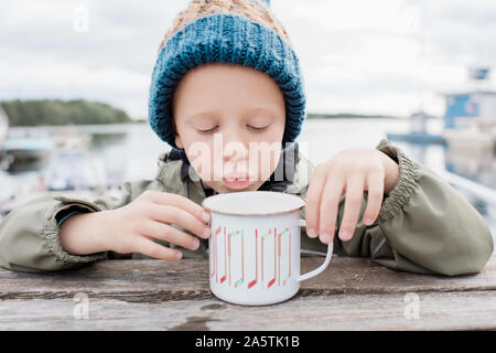 Jeune garçon de boire du chocolat chaud à l'extérieur, sur un banc de pique-nique en hiver Banque D'Images