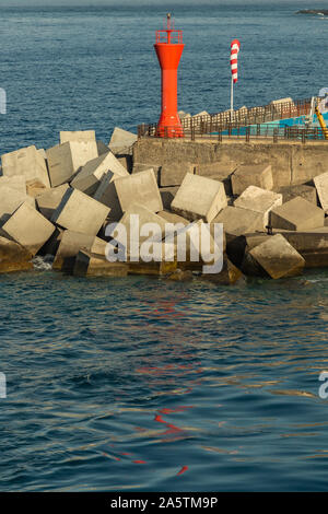 Phare rouge entouré de blocs de béton à l'extrémité de la jetée dans le port de Los Christianos à Ténérife. Vue depuis le ferry pour l'île de L Banque D'Images