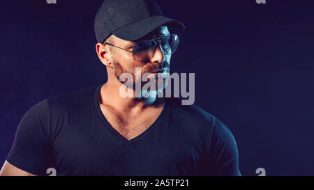 Portrait d'homme barbu brutale dans sunglassesand baseball cap à noir photo studio. Banque D'Images