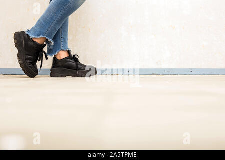 Femme avec blanc cuir chaussures de porter un jean bleu et des chaussures de sport autour de mur blanc Fashion Concept Banque D'Images