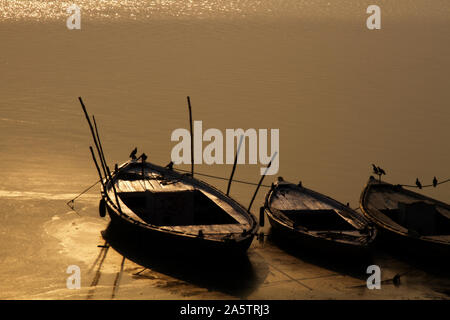 Magnifique coucher de soleil sur le Gange et calme bateaux amarrés au port, les poteaux de bambou coincé dans les côtés. Les pigeons ont volé à boire de l'eau Banque D'Images