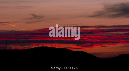 Coucher du soleil derrière une colline. Gros nuages de couleurs rouge et orange. Silhouettes noires de tours de radio sur la colline. Banque D'Images