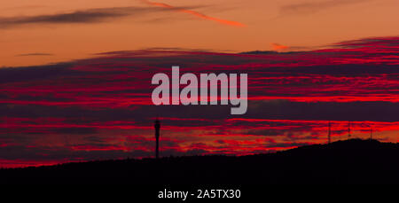 Coucher du soleil derrière une colline. Gros nuages de couleurs rouge et orange. Silhouettes noires de tours de radio sur la colline. Banque D'Images