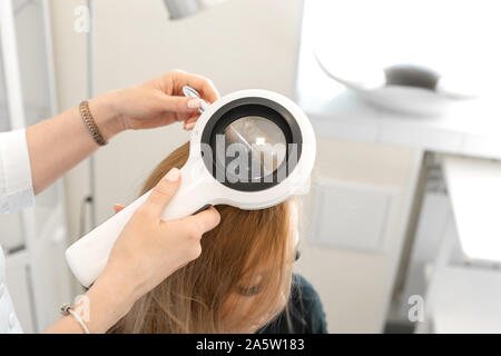 Un trichologist examine l'état des cheveux sur la tête des patients avec un dermatoscope. Dans une salle lumineuse cosmétologie. Banque D'Images