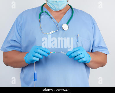 Médecin en uniforme bleu et des gants en latex est titulaire d'un système compte-gouttes en plastique pour injection intraveineuse, fond blanc Banque D'Images