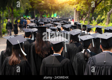 Vue arrière du groupe de diplômés universitaires en robes noires s'aligne pour le diplôme à l'université cérémonie de remise de diplômes. L'éducation Concept félicitations, stu Banque D'Images