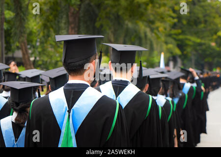 Vue arrière du groupe de diplômés universitaires en robes noires s'aligne pour le diplôme à l'université cérémonie de remise de diplômes. L'éducation Concept félicitations, stu Banque D'Images