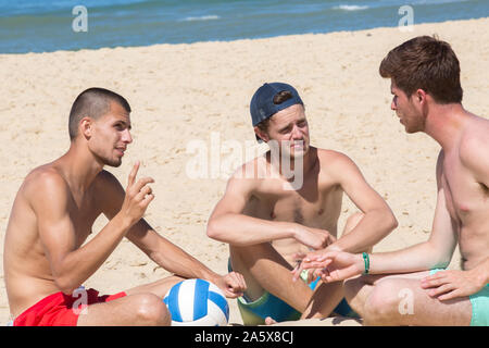 Trois hommes younf assis sur la plage Banque D'Images