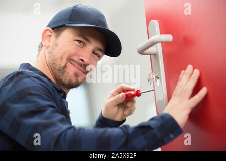 Heureux jeune menuisier installe avec serrure de porte tournevis sans fil Banque D'Images