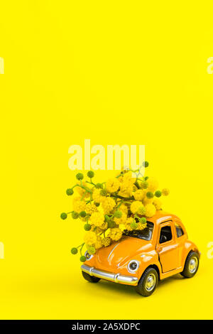 Moscou, Russie - le 23 février 2019 : 8 mars Journée internationale de la femme carte avec toy voiture rétro modèle de livrer bouquet de fleurs mimosa sur jaune Banque D'Images