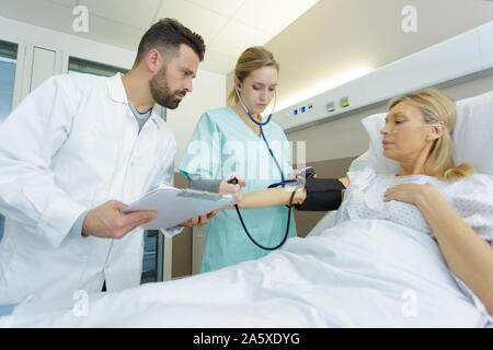 Caring doctor taking young womans hypertension in hospital bed Banque D'Images