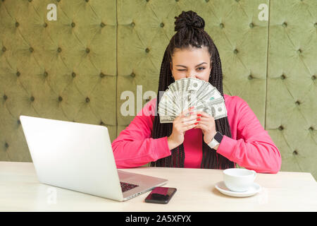 Portrait of attractive young adult businesswoman riche avec des dreadlocks hairstyle en chemisier rose est assis et montrant beaucoup de dollars en espèces, coverin Banque D'Images
