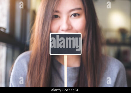 Une belle asian woman holding a blank blackboard carré signe avec l'arrière-plan flou Banque D'Images