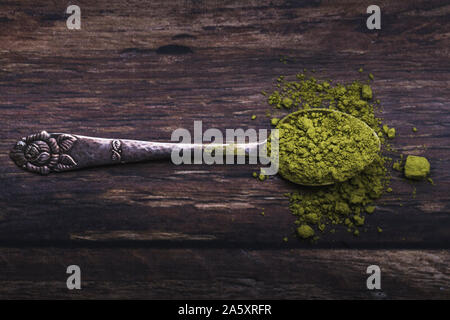 Une cuillère à motifs floral vintage Vert rempli de thé matcha en poudre. La cuillère est sur une vieille table en bois sombre. L'angle de la photo est droite fro Banque D'Images