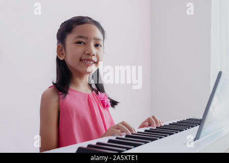 Un peu la fille asiatique jouant le clavier blanc avec bonheur. Les enfants portent une robe rose pratique du piano avec plaisir et sourire. Banque D'Images