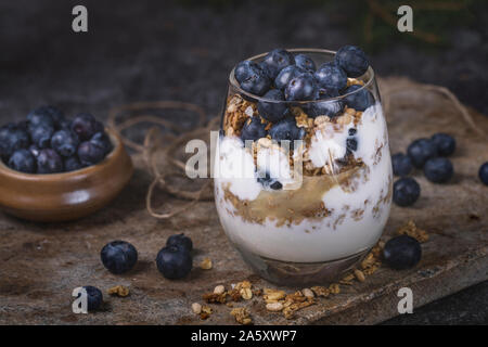 Un petit-déjeuner sain de yaourts, de muesli et de bleuets dans un verre. Le verre est porté sur une surface en pierre et à côté du verre est un petit nœud Banque D'Images