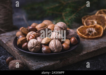 Noix Noël encore la vie. Une plaque brune avec une sélection de fruits entiers - les noix, noisettes, noix du Brésil et les amandes. Les écrous sont sur une pierre sombre ba Banque D'Images