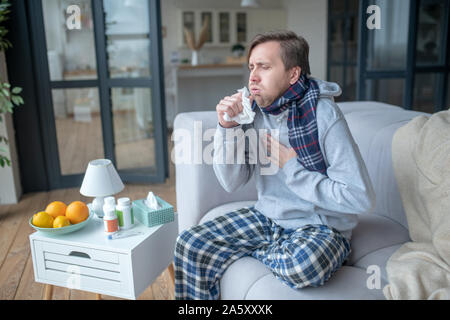 Homme assis sur un canapé et la toux après la prise des vitamines Banque D'Images