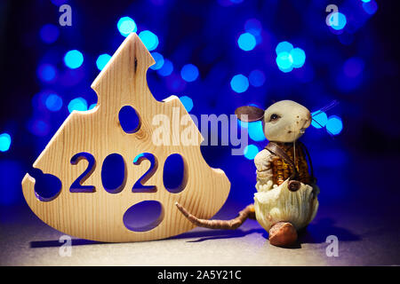 Carte de Nouvel An. L'année 2020 symbole de rat avec un morceau de fromage en bois bleu sur un arrière-plan flou. Les jouets, guirlandes. image horizontale. Banque D'Images