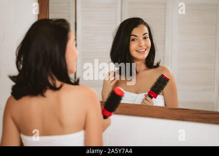 Gorgeous smiling woman brushing santé des cheveux devant le miroir. Fille peignant ses cheveux Banque D'Images