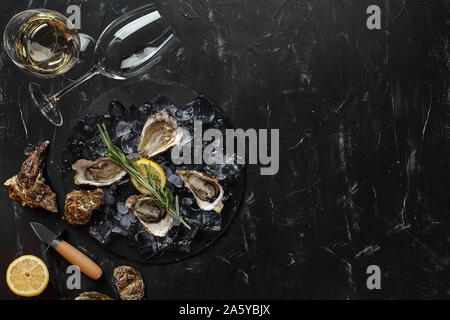 Fresh yummy a ouvert les huîtres, de la glace, du citron vert et un brin de lavande sur une ardoise ronde et deux verres de champagne sont sur une pierre noire zone texturée Banque D'Images