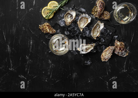 Fresh yummy a ouvert les huîtres, de la glace, du citron vert et un brin de lavande sur un rectangle de l'ardoise et deux verres de champagne sont sur une pierre noire ba texturé Banque D'Images