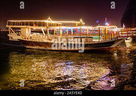 Bateaux boutre en bois, équipé de bandes de lumière, s'asseoir en attente de voitures tard le soir sur la Corniche de Doha Banque D'Images