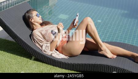 Femme avec téléphone piscine bleu près de se prélasser sur la terrasse de l'hôtel Banque D'Images