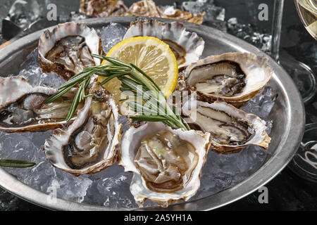 Fresh yummy a ouvert les huîtres, de la glace, du citron vert et un brin de lavande sur une plaque de métal ronde, black stone background. Souper avec champagne à Banque D'Images