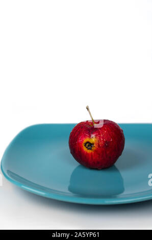 Rotten apple rouge sur une plaque, turquoise sur fond blanc Banque D'Images