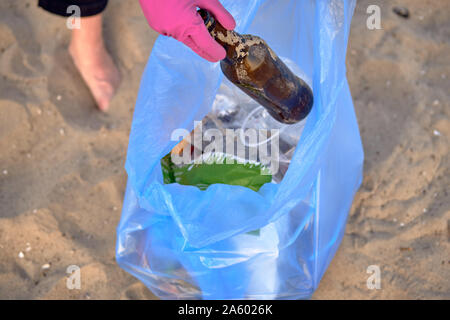 Bénévole responsable en violet gants de caoutchouc est la marche avec sac à déchets le long d'une côte de la rivière sale et le nettoyage de la corbeille. Les gens et l'écologie. Banque D'Images