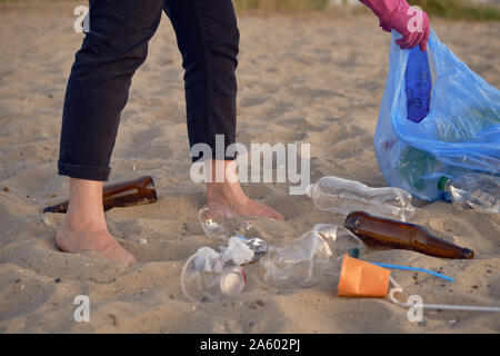 Les jeunes responsables de l'est de marcher avec un sac poubelle bleu le long d'une plage de la rivière sale et le nettoyage des déchets anciens, bouteilles en verre et en plastique, des tasses Banque D'Images