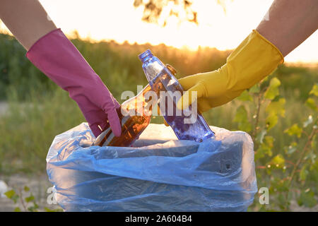 Les jeunes conscients en violet et jaune des gants de caoutchouc sont à pied avec des sacs poubelles le long d'une zone verte d'une sale côte de la rivière et de nettoyage Banque D'Images