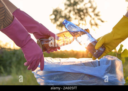 Les jeunes responsables en violet et jaune des gants de caoutchouc sont à pied avec des sacs poubelles le long d'une zone verte d'une sale côte de la rivière et cleanin Banque D'Images