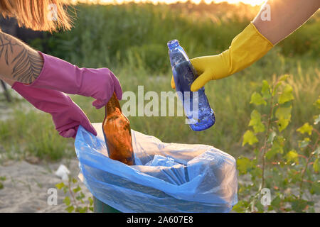 Les jeunes volontaires en violet et jaune des gants de caoutchouc sont à pied avec des sacs poubelles le long d'une zone verte d'une sale côte de la rivière et le nettoyage de tra Banque D'Images