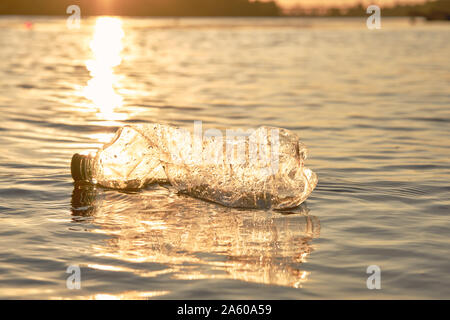 Bouteille de plastique flotte à la surface de l'eau. Coucher du soleil, le vert des arbres. Les gens et l'écologie. La pollution de la rivière. La préservation de la nature. Voluntee Banque D'Images