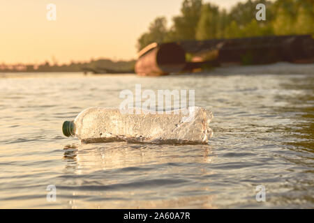 Bouteille en plastique froissés flotte à la surface de l'eau. Coucher du soleil, le vert des arbres. Les gens et l'écologie. La pollution de la rivière. La préservation de la nature. Volon Banque D'Images