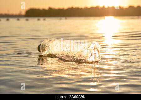 Bouteille de plastique froissé flotte à la surface de l'eau. Coucher du soleil, le vert des arbres. Les gens et l'écologie. La pollution de la rivière. La préservation de la nature. Volu Banque D'Images