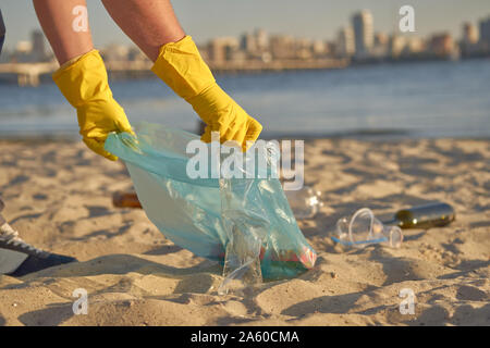 Responsable Guy en gants jaunes marche avec sac à déchets le long d'un bord de l'eau sale du fleuve et le nettoyage de la corbeille. La pollution de la rivière. Volunte Banque D'Images