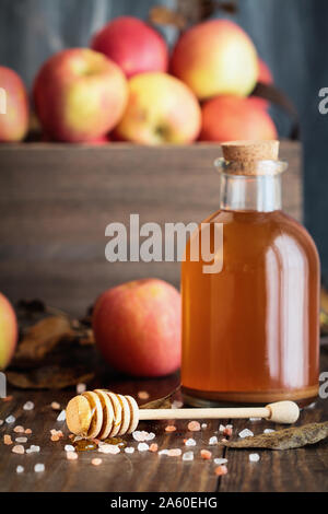 Balancier avec miel miel rose entouré de sel de l'himalaya. Le vinaigre de cidre de pomme, avec la mère, et des pommes fraîches sont à l'arrière-plan. Foc sélective Banque D'Images