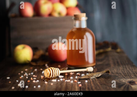 Balancier avec miel miel rose entouré de sel de l'himalaya. Le vinaigre de cidre de pomme, avec la mère, et des pommes fraîches sont à l'arrière-plan. Foc sélective Banque D'Images