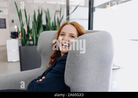 Rousse Happy businesswoman sitting in armchair Banque D'Images