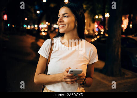 Young woman using smartphone dans la ville la nuit Banque D'Images