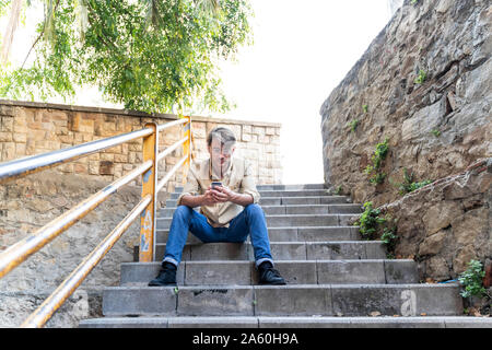 Homme assis sur un escalier extérieur using cell phone Banque D'Images