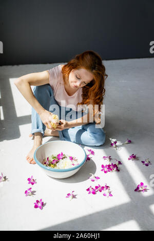 Femme rousse assise sur le sol avec bol d'orchid blossom et éponge naturelle Banque D'Images