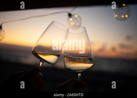 Femme tenant deux verres de vin blanc en van au coucher du soleil Banque D'Images