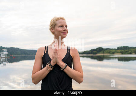 Jeune femme aux mains jointes à un lac Banque D'Images