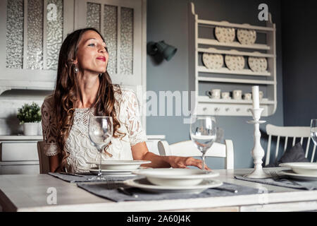 Jeune femme souriant assis à table dans la cuisine de style campagnard Banque D'Images