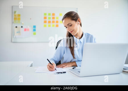 Young businesswoman préparer des documents tout en travaillant avec laptop in office Banque D'Images